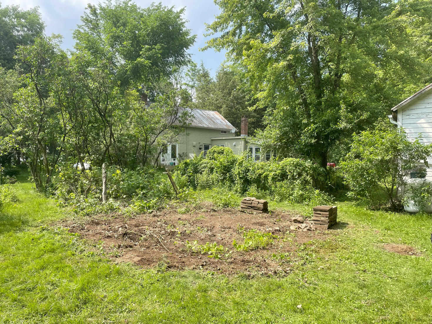 After: A garden bed cleared out with pavers stacked neatly in two spots. A house can be seen in the background